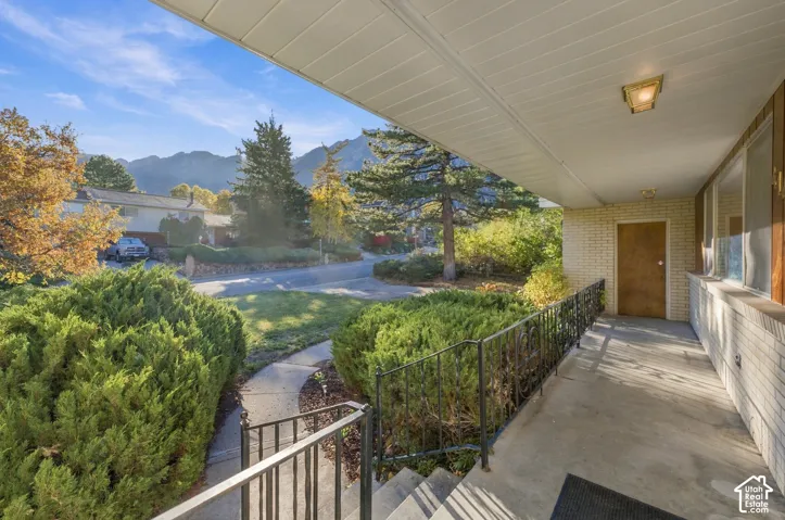 Covered front porch featuring a concrete foundation, decorative wrought-iron railing, brick exterior cladding, and mountain scenery