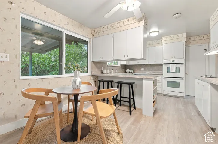 Kitchen featuring white cabinetry, light-toned solid surface countertops, built-in double wall oven, and wood-finish flooring