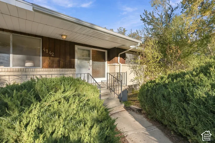 Exterior facade featuring a combination of brick masonry and vertical wood-finish siding, recessed covered entryway, wrought iron handrails, and mature foundation plantings