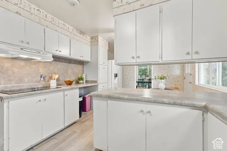 Kitchen featuring white cabinetry, stone-finish countertops, an integrated cooktop, a built-in range hood, and wood-finish flooring