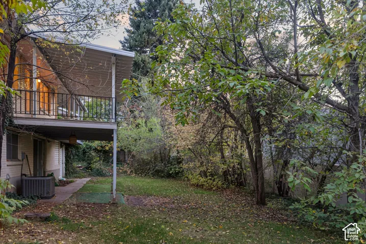 Elevated balcony with metal railing, covered patio, brick exterior, and mature landscape