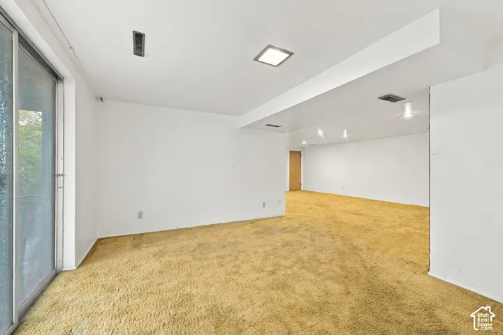 Expansive interior space featuring wall-to-wall carpeting, recessed square lighting fixtures, and a glass sliding door