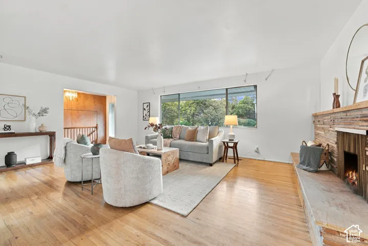 Living room featuring wood-finish flooring, a wood-paneled fireplace surround, an extended stone hearth, and a large picture window