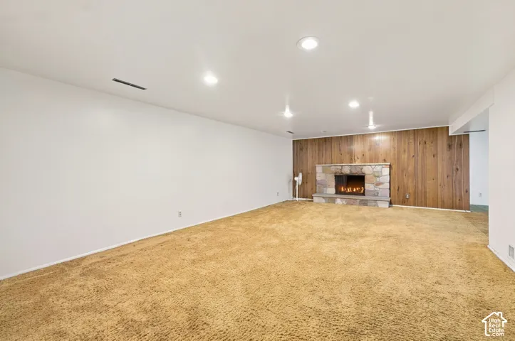 Open living area featuring recessed lighting, carpeted flooring, wood-paneled accent wall, and a stone fireplace with a raised hearth