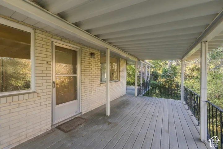 Covered outdoor deck featuring light-colored brick siding, aluminum roofing, and black wrought iron railing