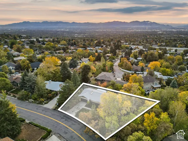 Single-story residence featuring a paved driveway, attached garage, and a lot with mature trees and mountain backdrops