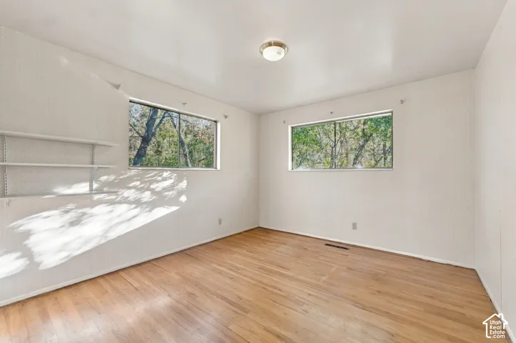 Room featuring wood-finish flooring, two sliding windows with exterior greenery, built-in wall shelving, and a flush-mount ceiling light