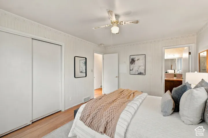 Bedroom featuring vertical beadboard paneling, wood-finish flooring, ceiling fan with integrated light fixture, and dual-panel sliding closet doors