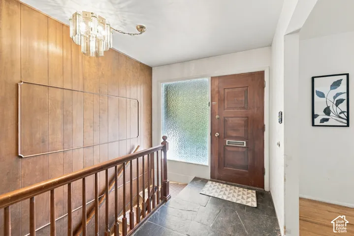 Foyer featuring natural stone tile flooring, wood paneling, a multi-paneled wood entry door, textured glass sidelight, and an intricate tiered glass chandelier