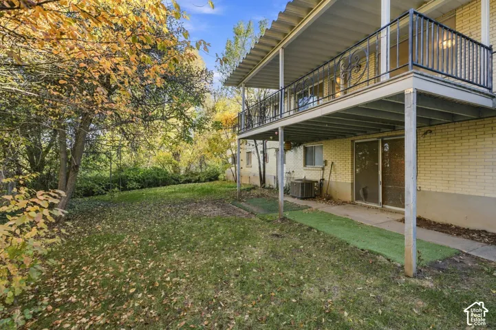 Exterior brick facade with a covered patio, featuring an elevated balcony with black metal railings and mature trees