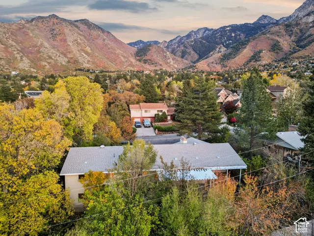 Aerial perspective of a multi-level residence featuring a pitched roof, an attached patio cover, and extensive mature trees set against a prominent mountain range