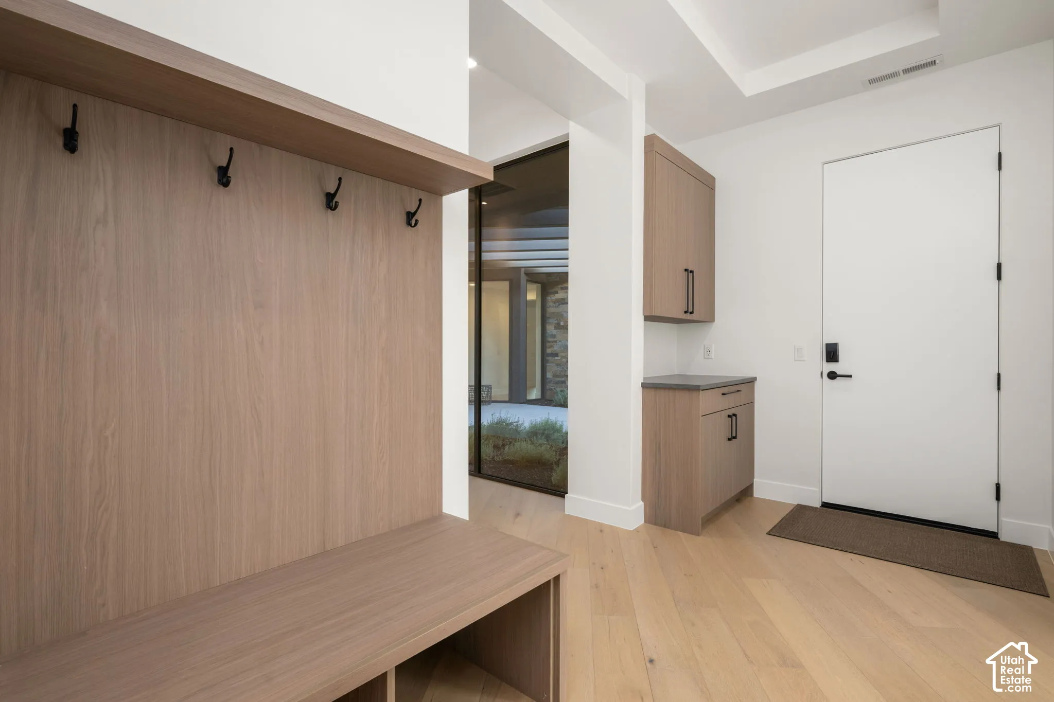 Built-in wood-finish cabinetry featuring upper and lower storage, integrated bench seating with coat hooks, and wide-plank wood-finish flooring