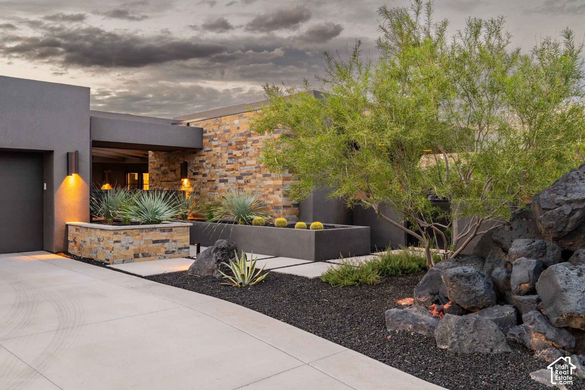 Modern exterior featuring stone veneer siding, smooth-finish stucco, built-in concrete planters, and desert-inspired landscaping with rock formations