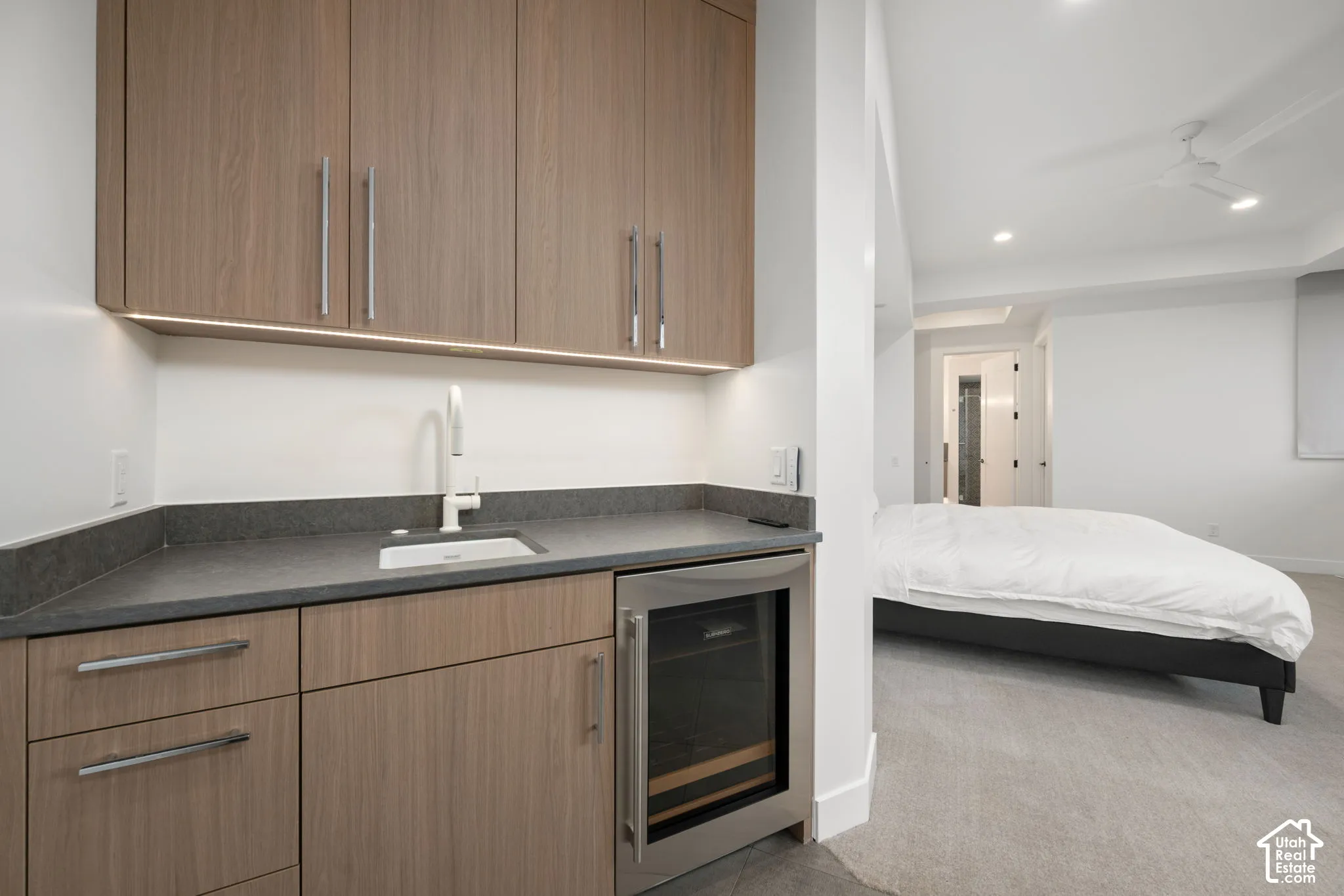 Built-in wet bar featuring wood-finish cabinetry, dark solid-surface countertop, under-cabinet lighting, integrated beverage refrigerator, and gooseneck faucet