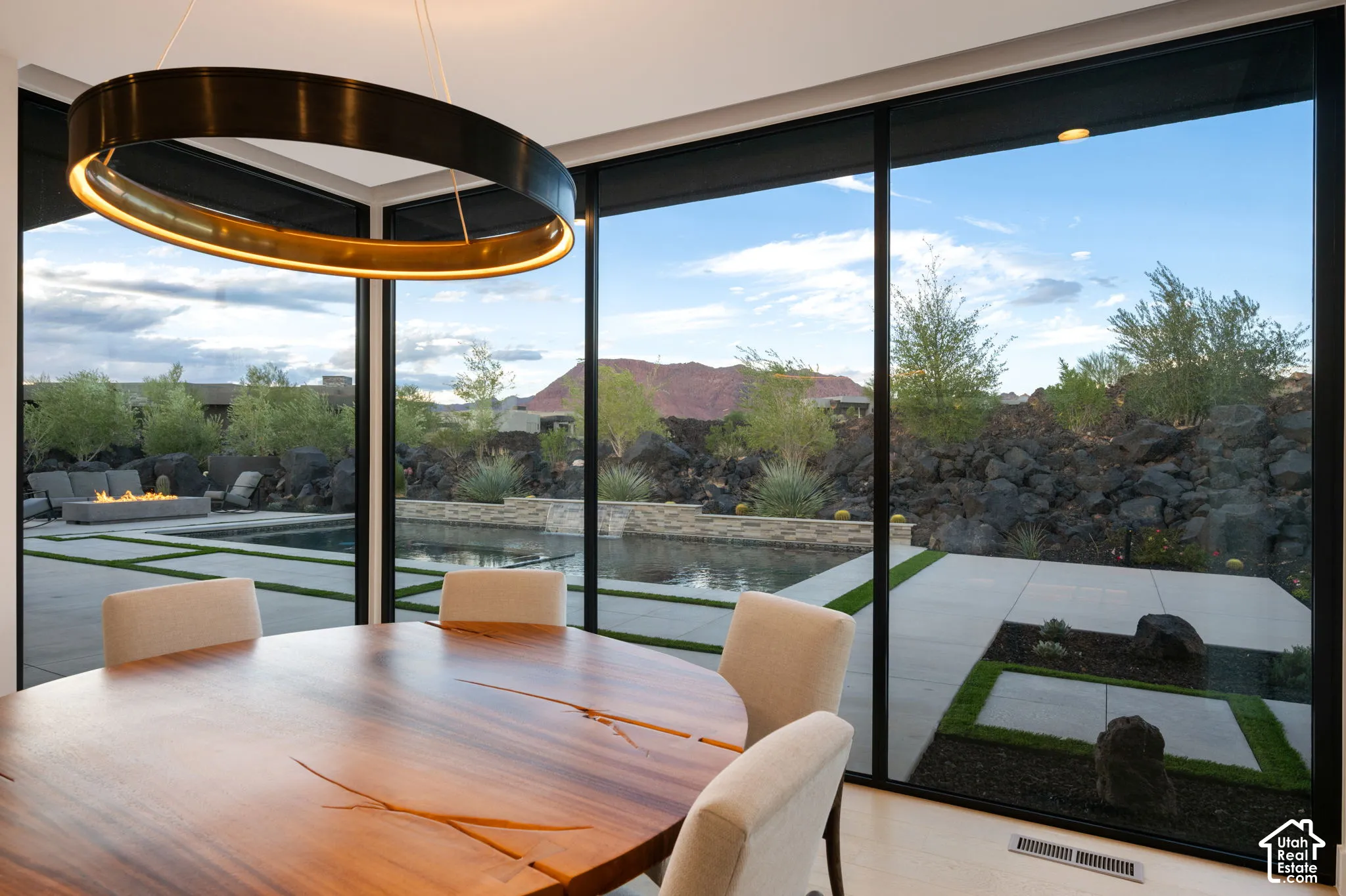 Floor-to-ceiling windows featuring black framing, circular pendant lighting, and direct exterior visibility of a hardscaped patio, swimming pool, and mountain backdrop