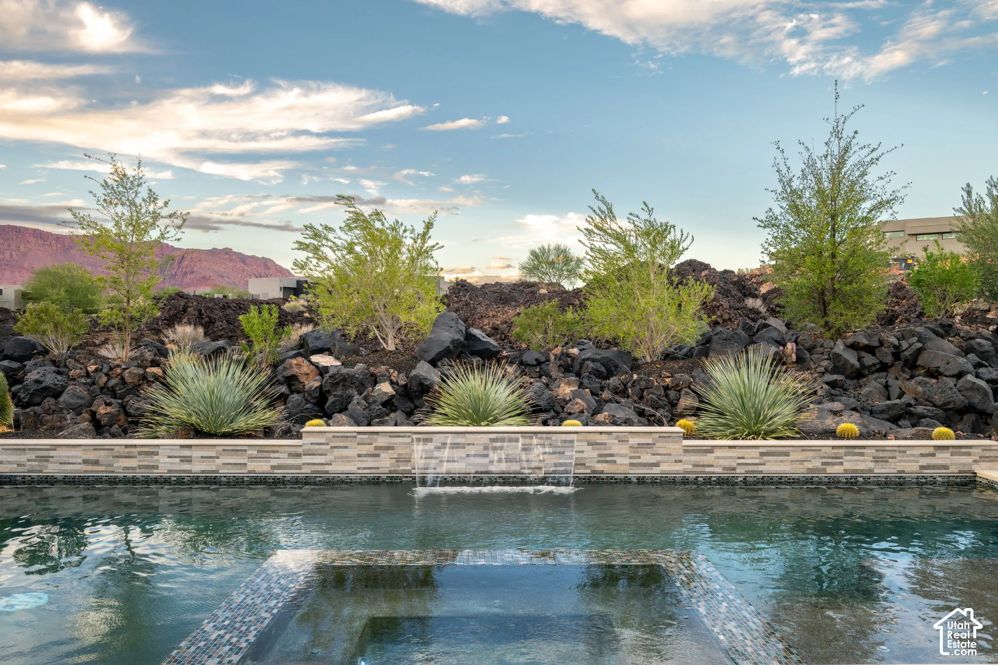 Swimming pool with a tile-trimmed spa, integrated water feature, stacked stone retaining wall, and desert landscaping