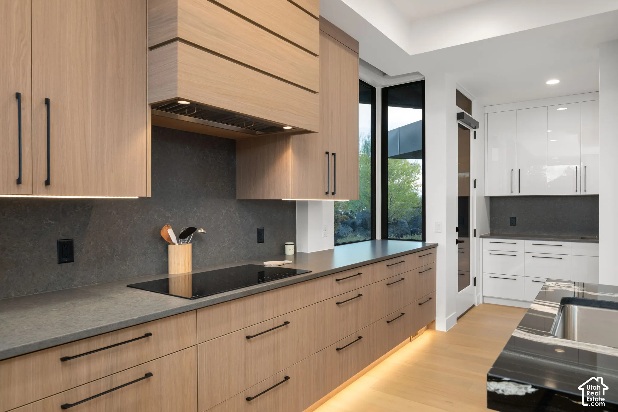 Kitchen featuring custom wood cabinetry, integrated range hood, matte black hardware, stone-finish countertops, and wood-finish flooring