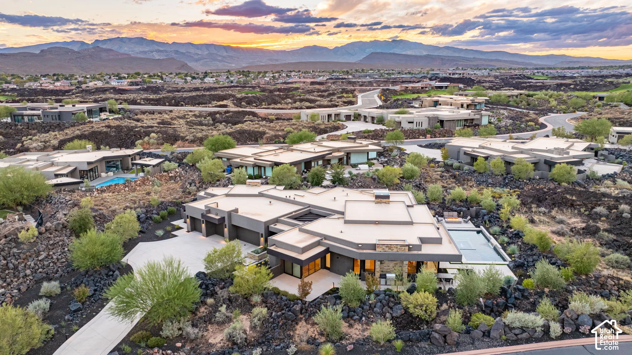 Modern desert architectural exterior featuring flat roof lines, stacked stone accents, multi-car garage, private swimming pool, and mountain backdrop