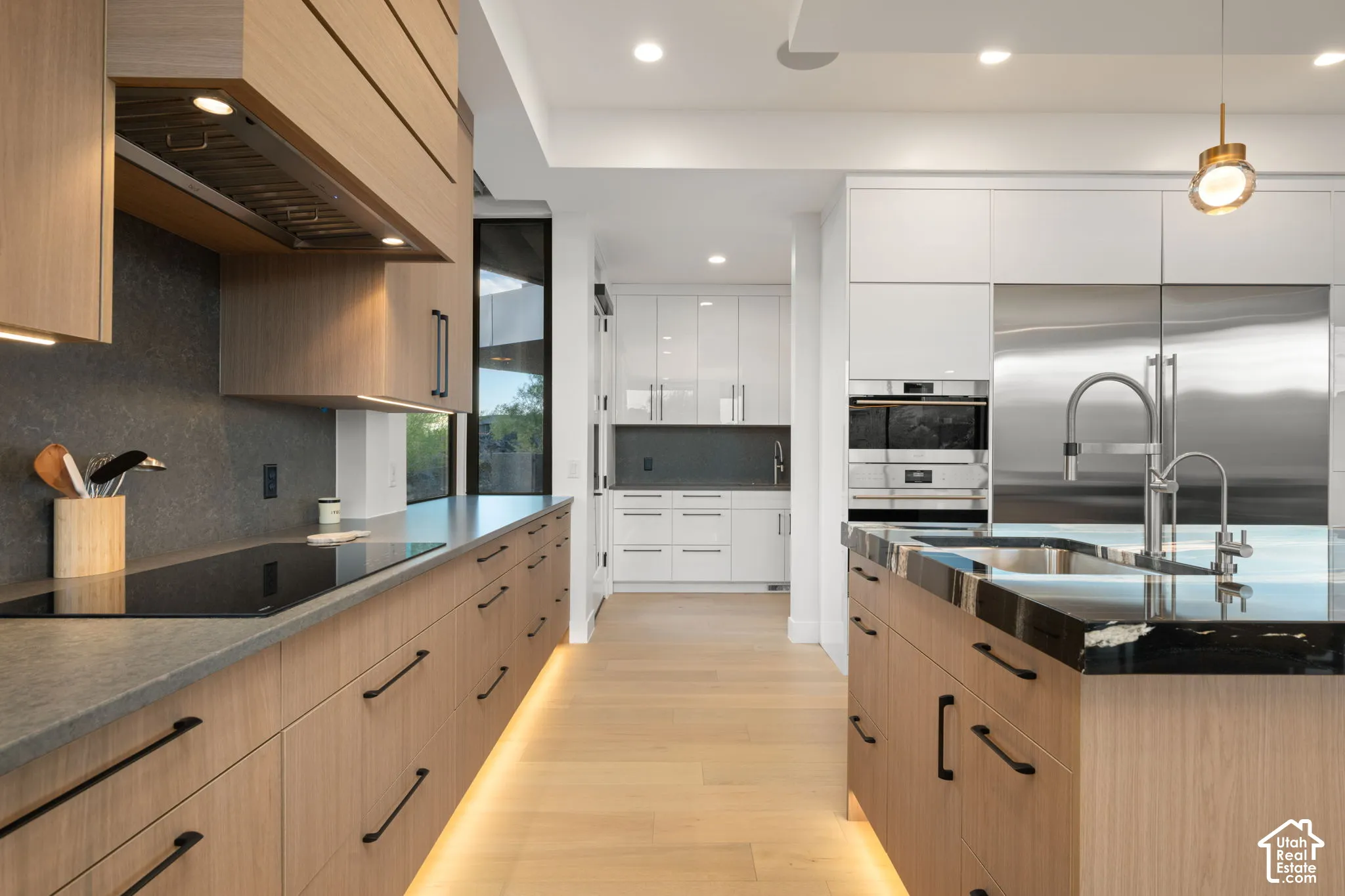 Modern kitchen featuring matte wood-finish cabinetry, white high-gloss upper cabinets, solid-surface countertops with a natural stone-style backsplash, integrated stainless steel appliances, and under-cabinet toe-kick lighting