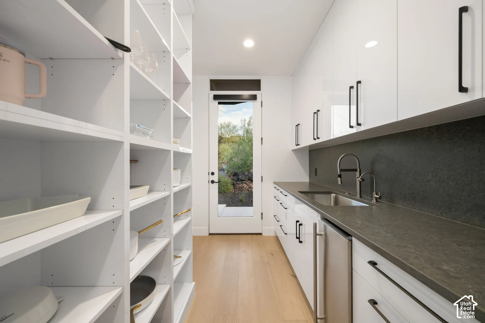 Pantry featuring white cabinetry with matte black hardware, stone-finish countertops, wood-finish flooring, integrated sink, and glass-paneled exterior door