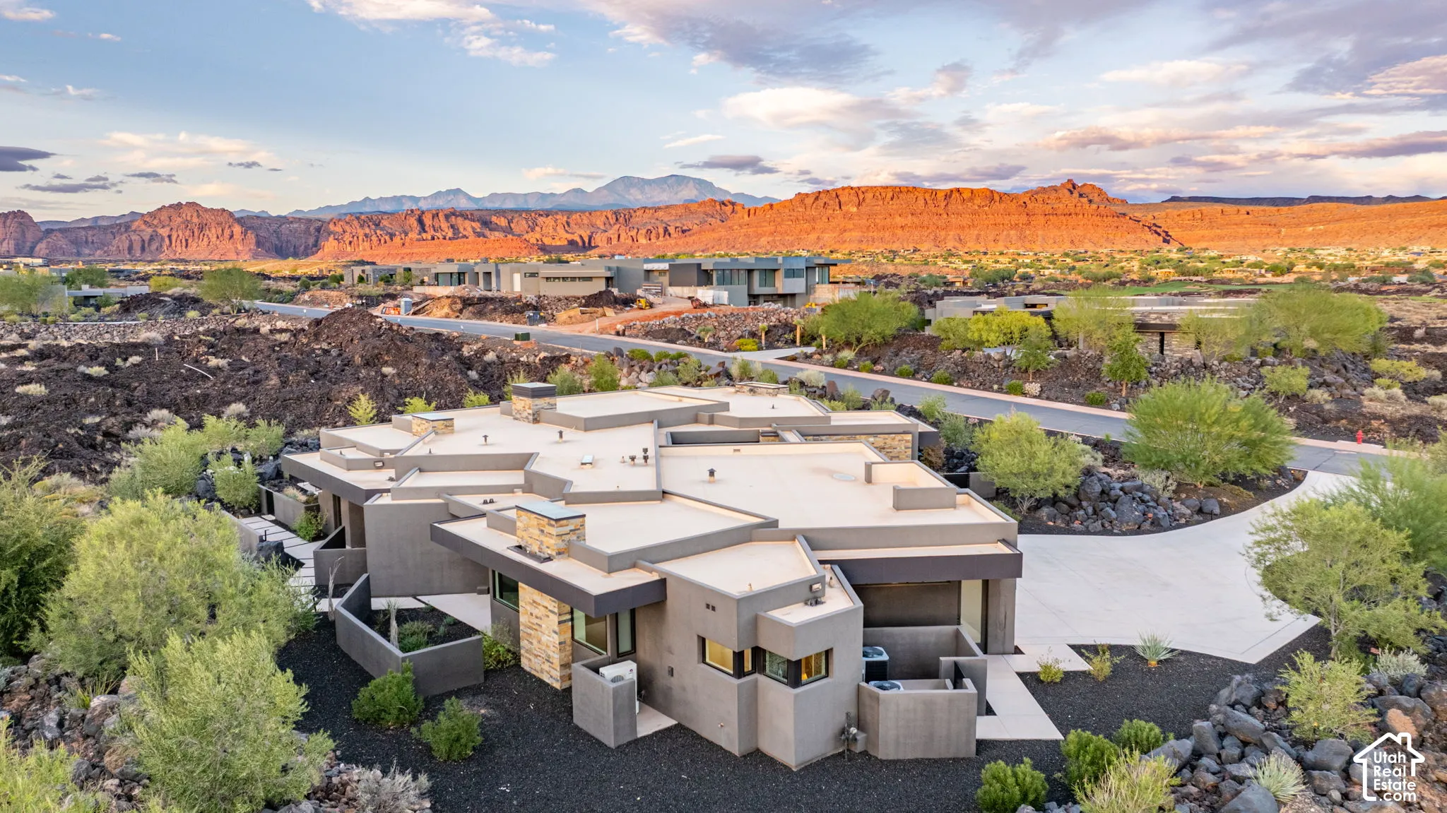Modern architectural exterior with multi-level flat rooflines, stone-veneer chimney, concrete driveway, and natural landscape backdrop of rock formations