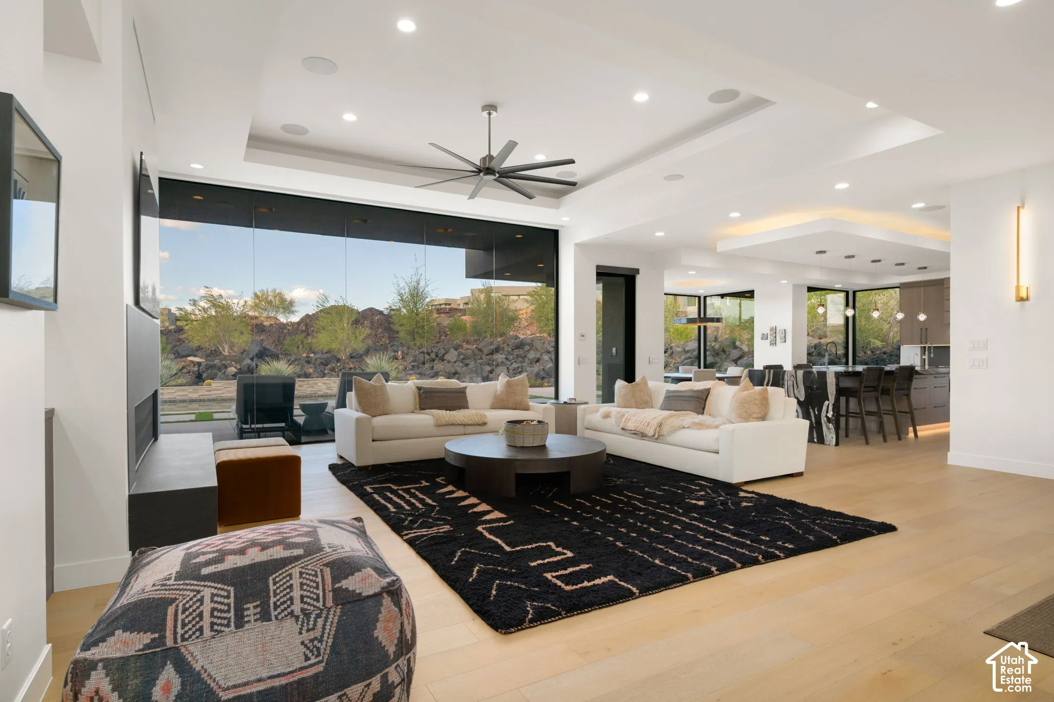 Open-concept interior featuring wood-finish flooring, recessed lighting, a tray ceiling with a multi-blade ceiling fan, and floor-to-ceiling glass panel walls