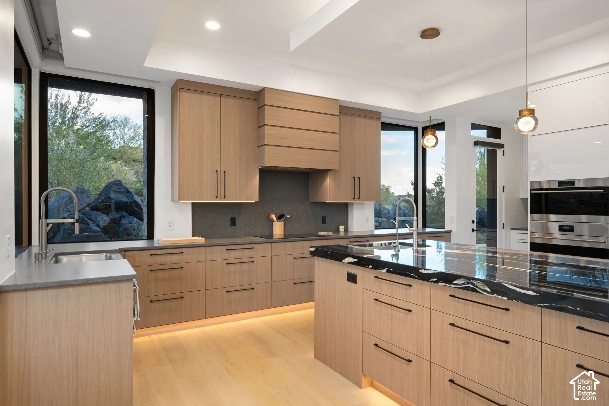 Kitchen featuring wood-finish cabinetry, a contrasting stone-topped island, built-in stainless steel double ovens, integrated range hood, and wood-finish flooring