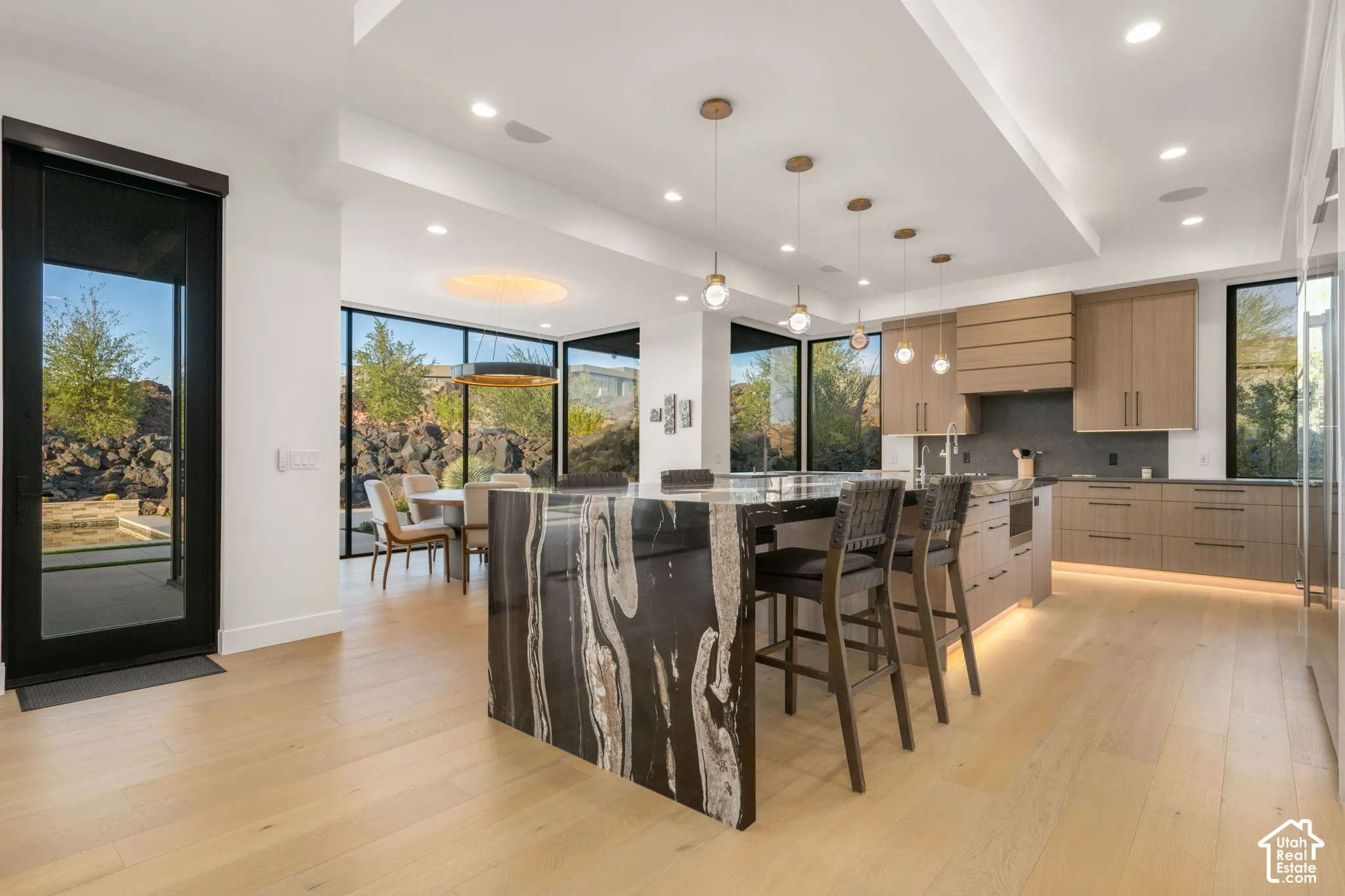 Kitchen featuring a waterfall-edge island with stone detailing, custom wood-finish cabinetry, recessed lighting, drop pendant fixtures, and floor-to-ceiling windows