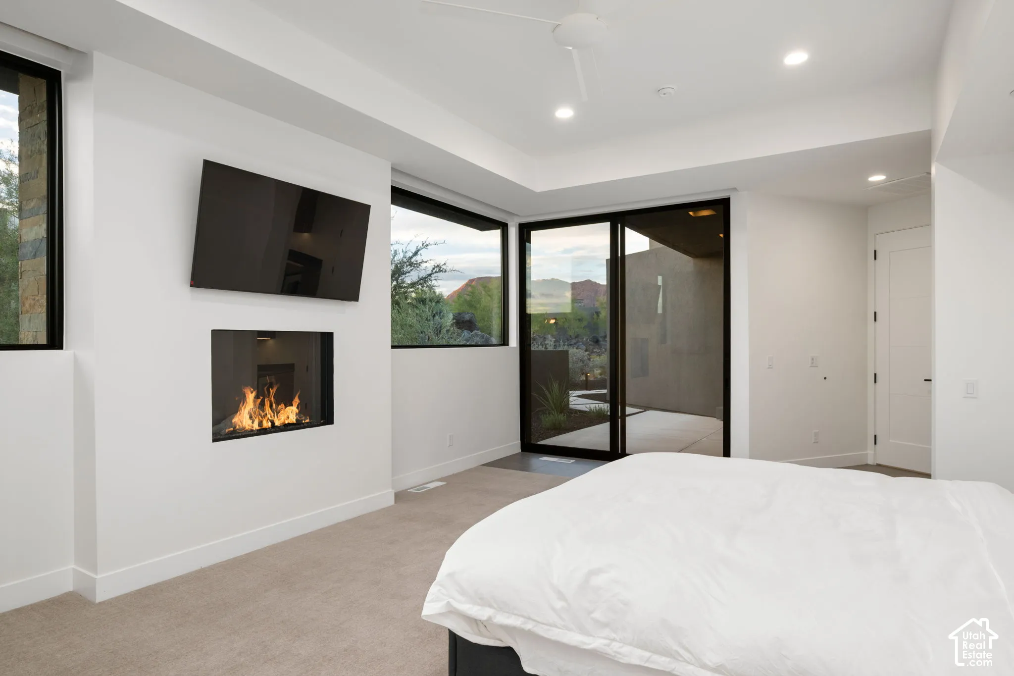 Recessed fireplace with stone surround, large-format sliding glass door, high ceilings with recessed lighting, and wall-to-wall carpeting