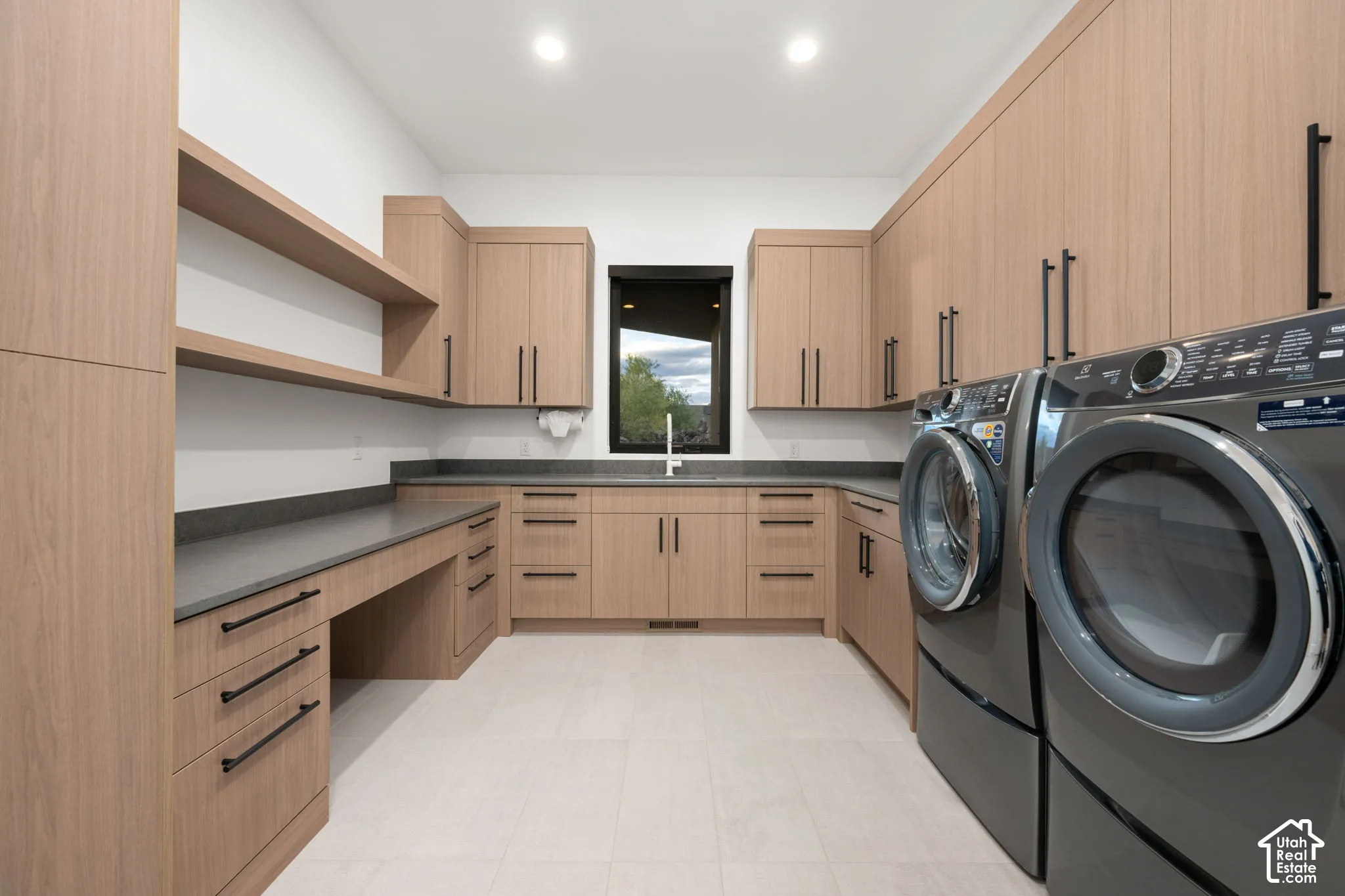 Custom wood-finish cabinetry featuring matte black hardware, stone-composite countertops, built-in open shelving, an undermount sink with a gooseneck faucet, and light-toned tile flooring