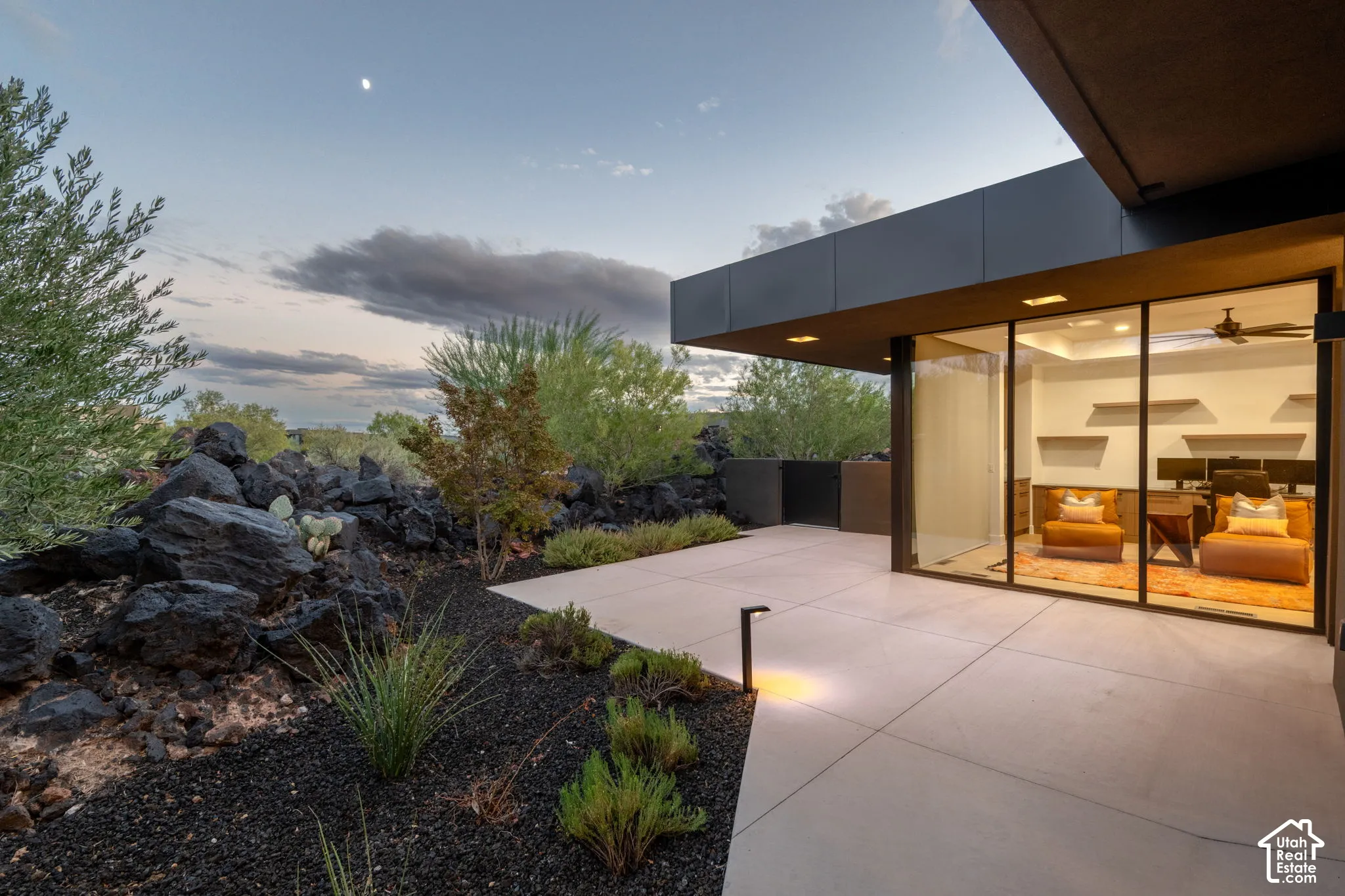 Modern architectural exterior featuring expansive concrete patio, floor-to-ceiling glass wall, rock landscaping, and built-in wall shelving