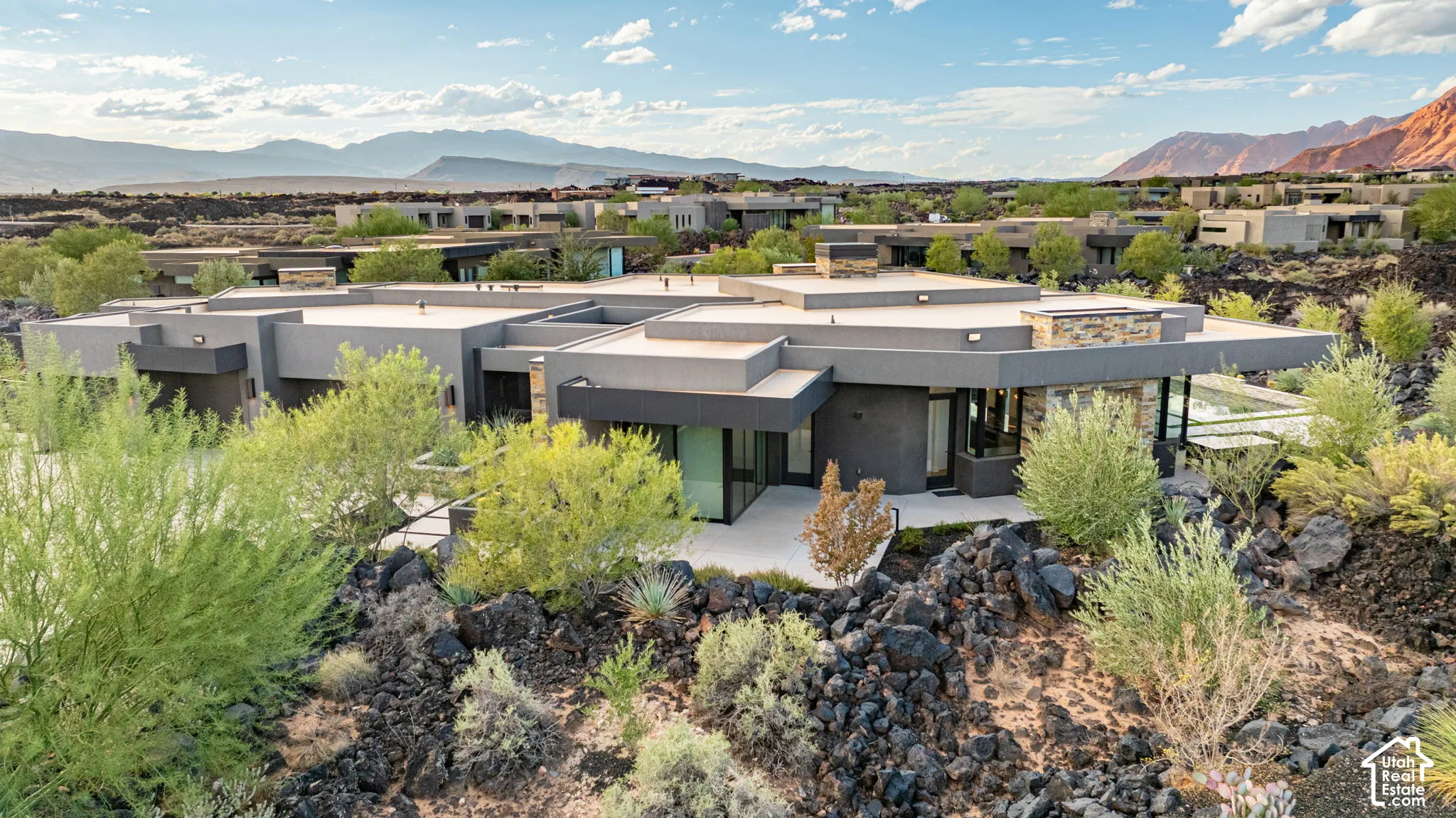 Modern architectural residence featuring a flat roofline, stone veneer accents, multi-level exterior composition, and native desert landscaping