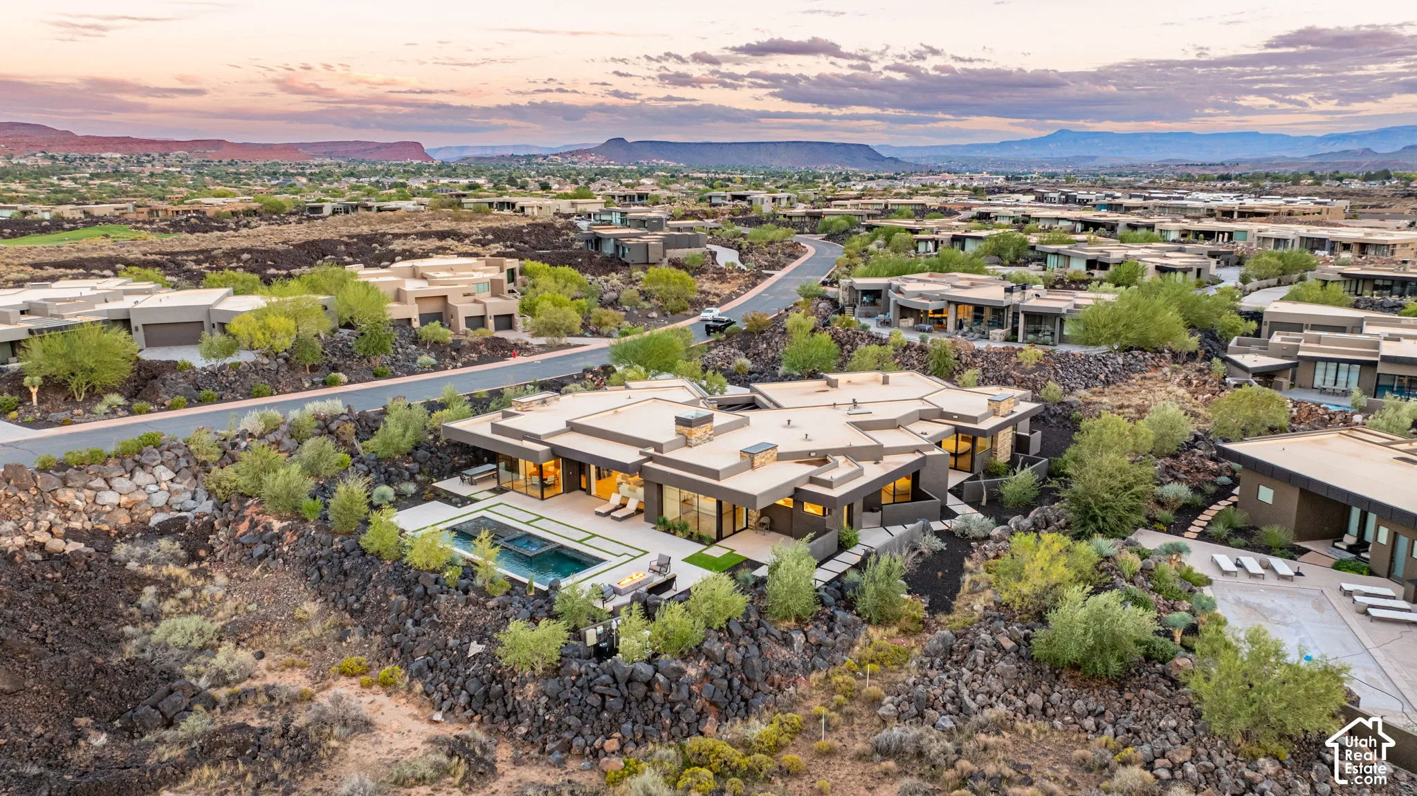 Contemporary residence featuring a low-profile flat roofline, integrated swimming pool with spa, expansive patio hardscaping, and prominent volcanic rock landscaping