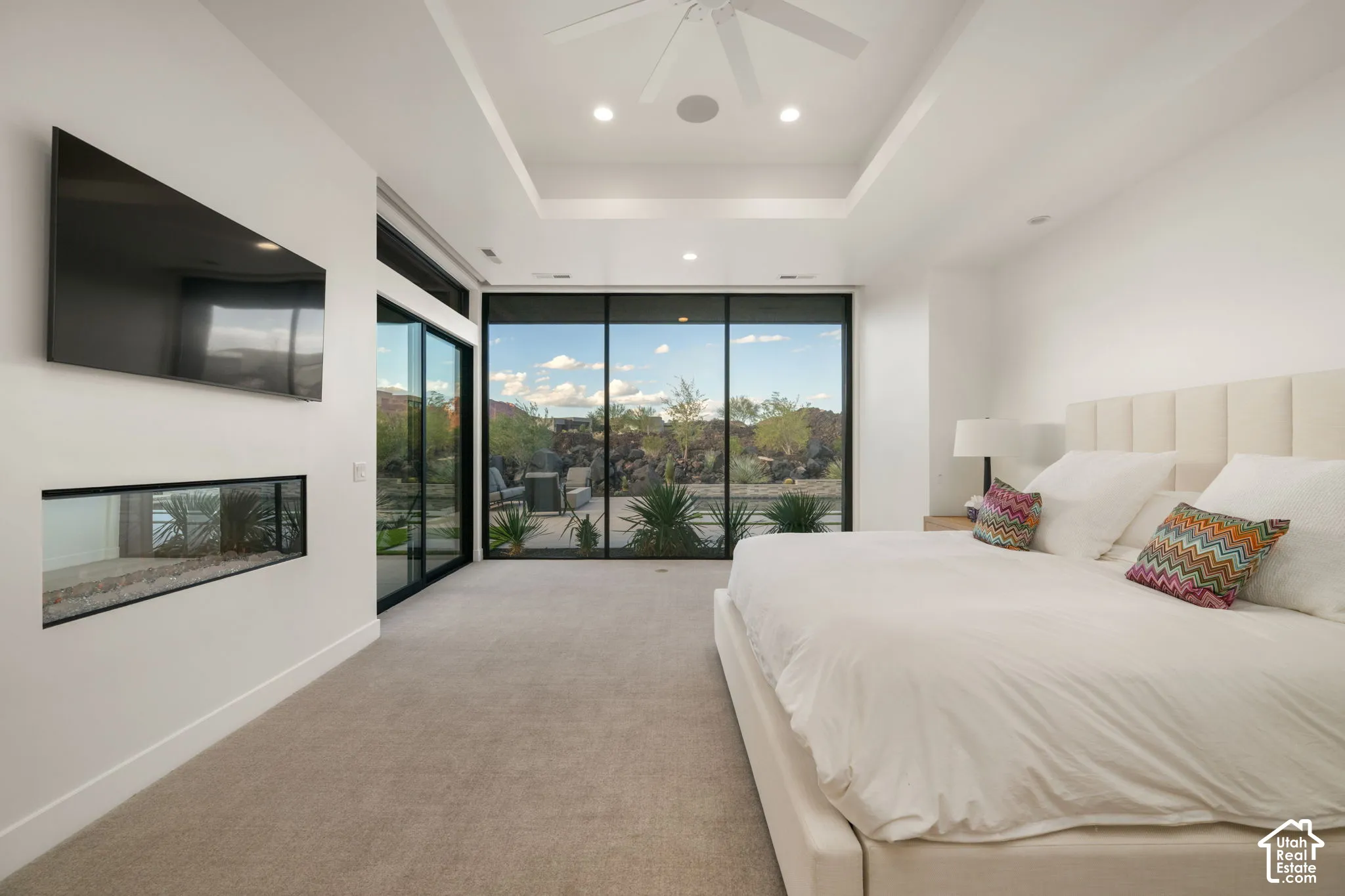 Floor-to-ceiling glass walls, recessed tray ceiling, built-in horizontal fireplace, neutral carpeting, and integrated ceiling lighting