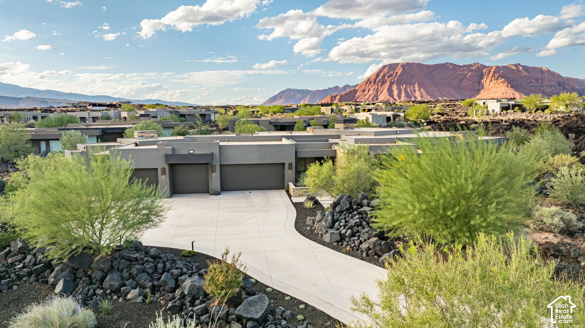 Modern single-story exterior featuring a multi-car garage, concrete driveway, stone rockscape landscaping, and mountain backdrop