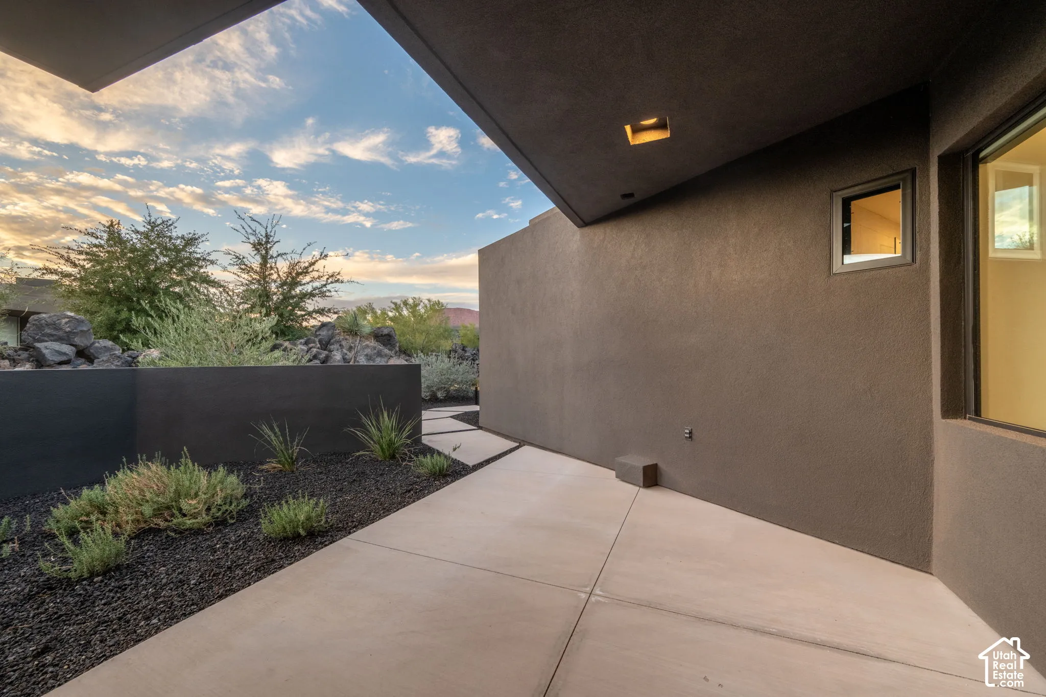 Covered patio featuring concrete flooring, stucco walls, recessed lighting, and a landscaped rock garden