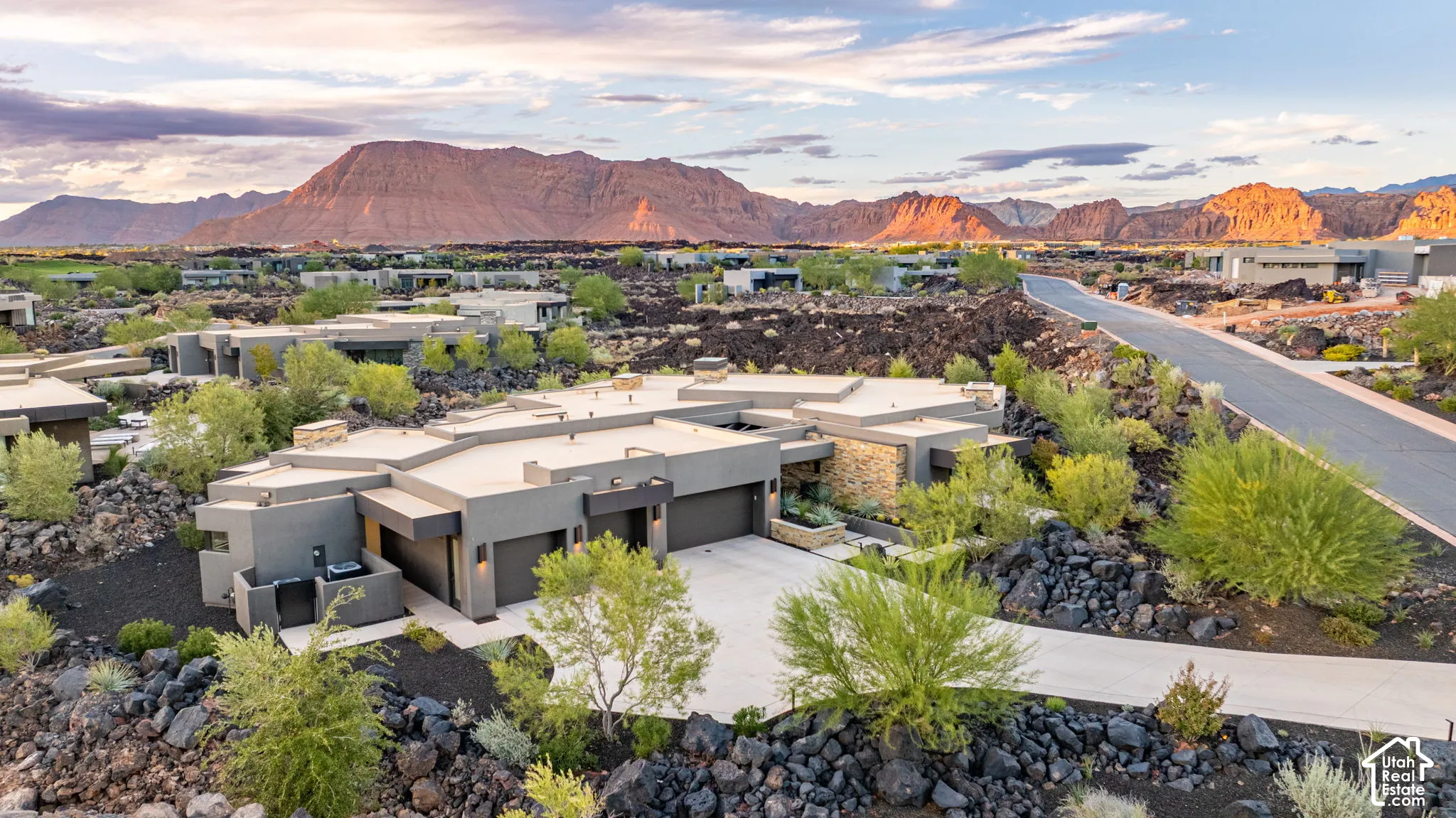 Contemporary residence featuring a low-profile exterior, stone masonry accents, a multi-car garage, and a concrete driveway, set against a desert mountain backdrop