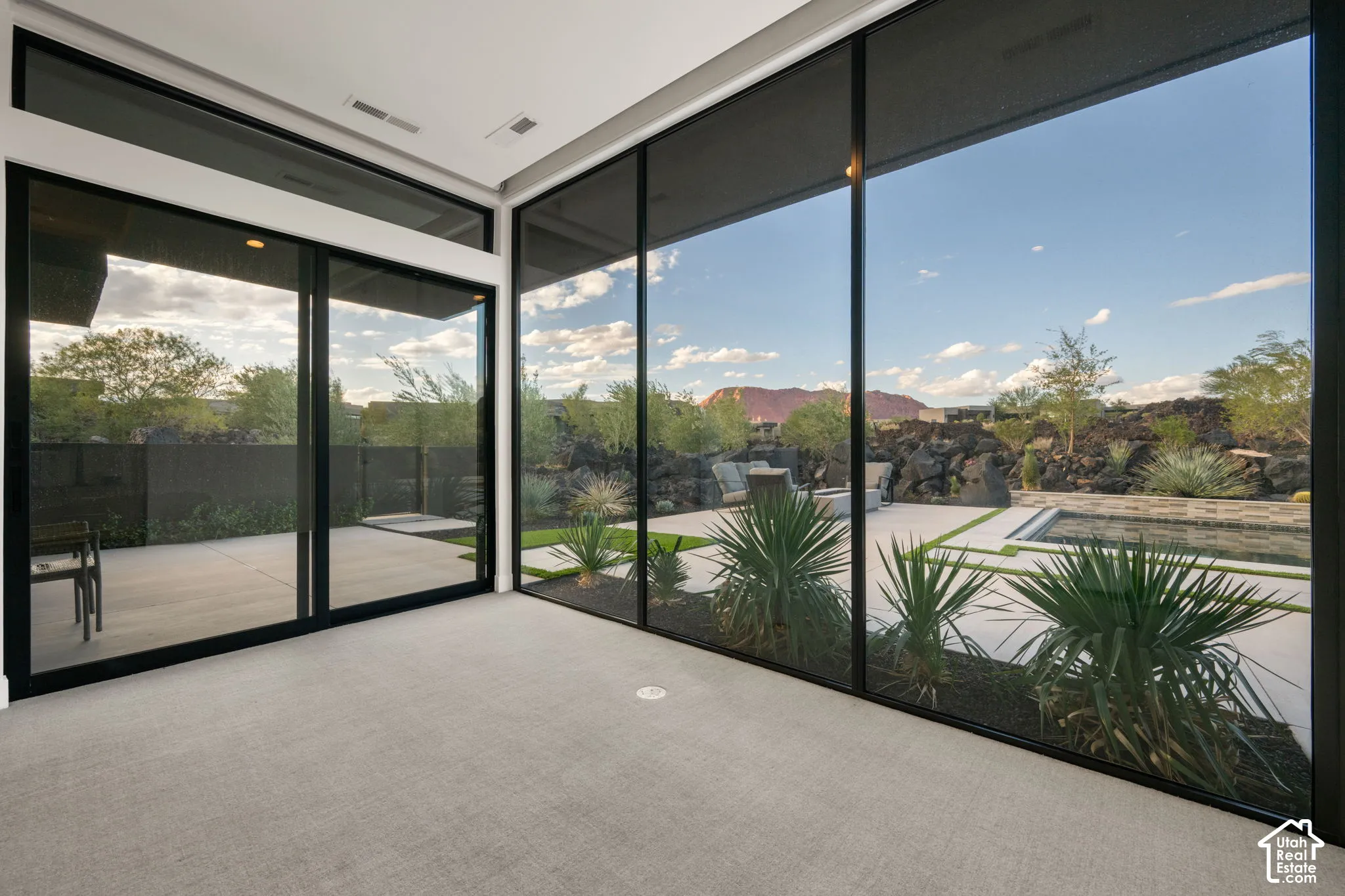 Floor-to-ceiling sliding glass walls, expansive concrete patio with built-in pool, and desert landscaping set against a mountain backdrop