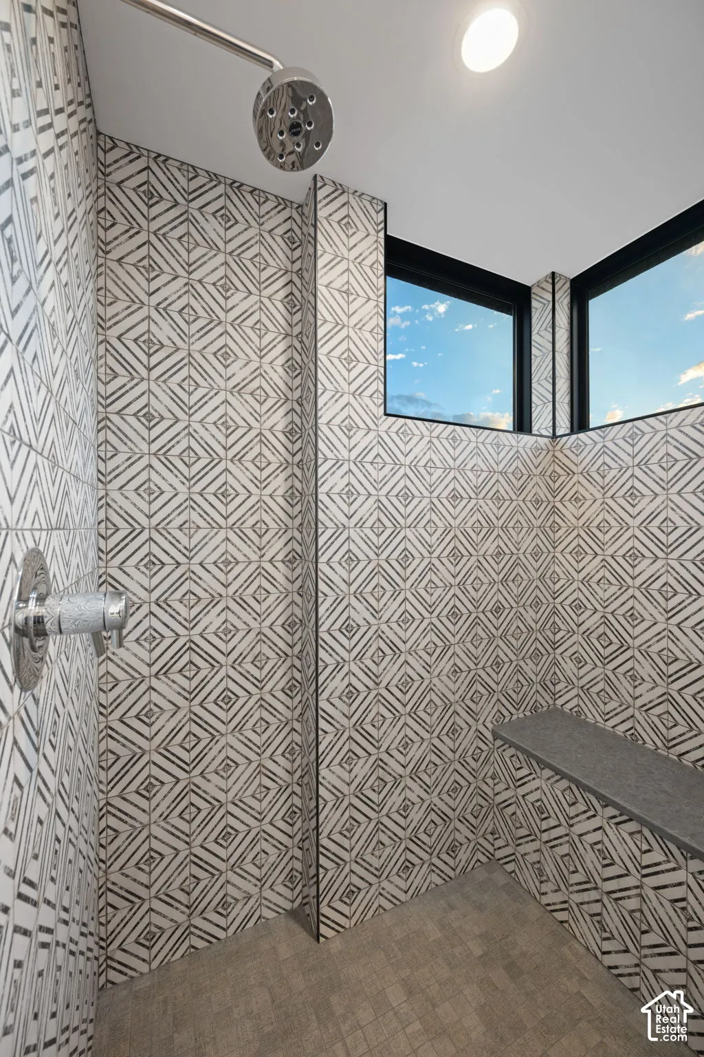 Walk-in shower featuring geometric patterned wall tile, a built-in stone bench, corner windows with black frames, and polished chrome plumbing fixtures