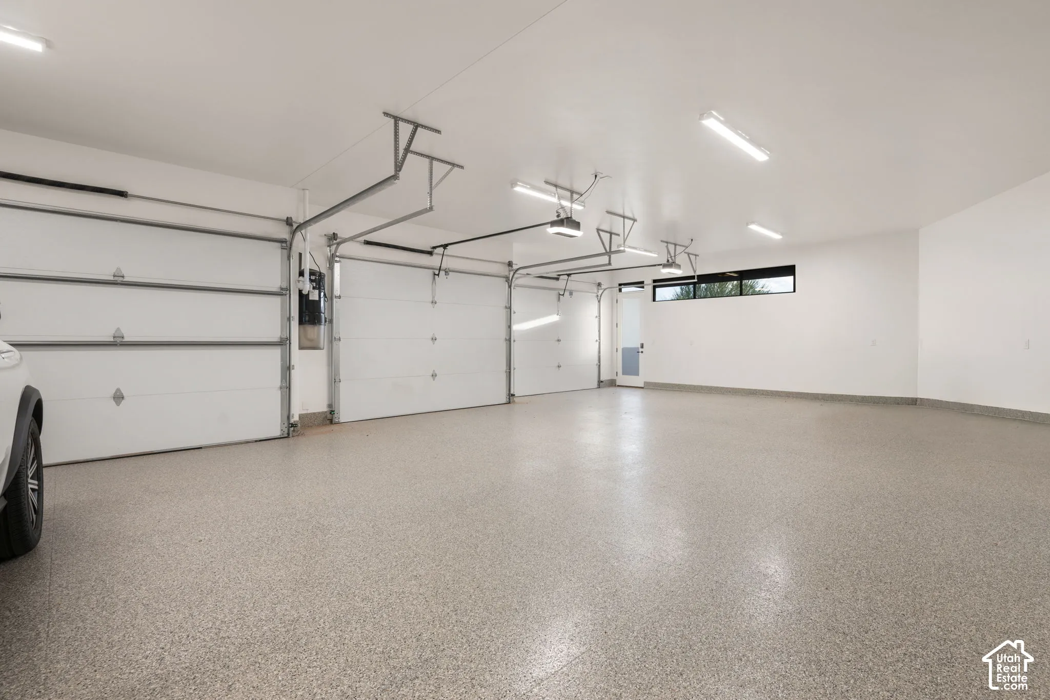 Three-car garage featuring epoxy-coated flooring, white interior walls, overhead LED lighting, and a single pedestrian door