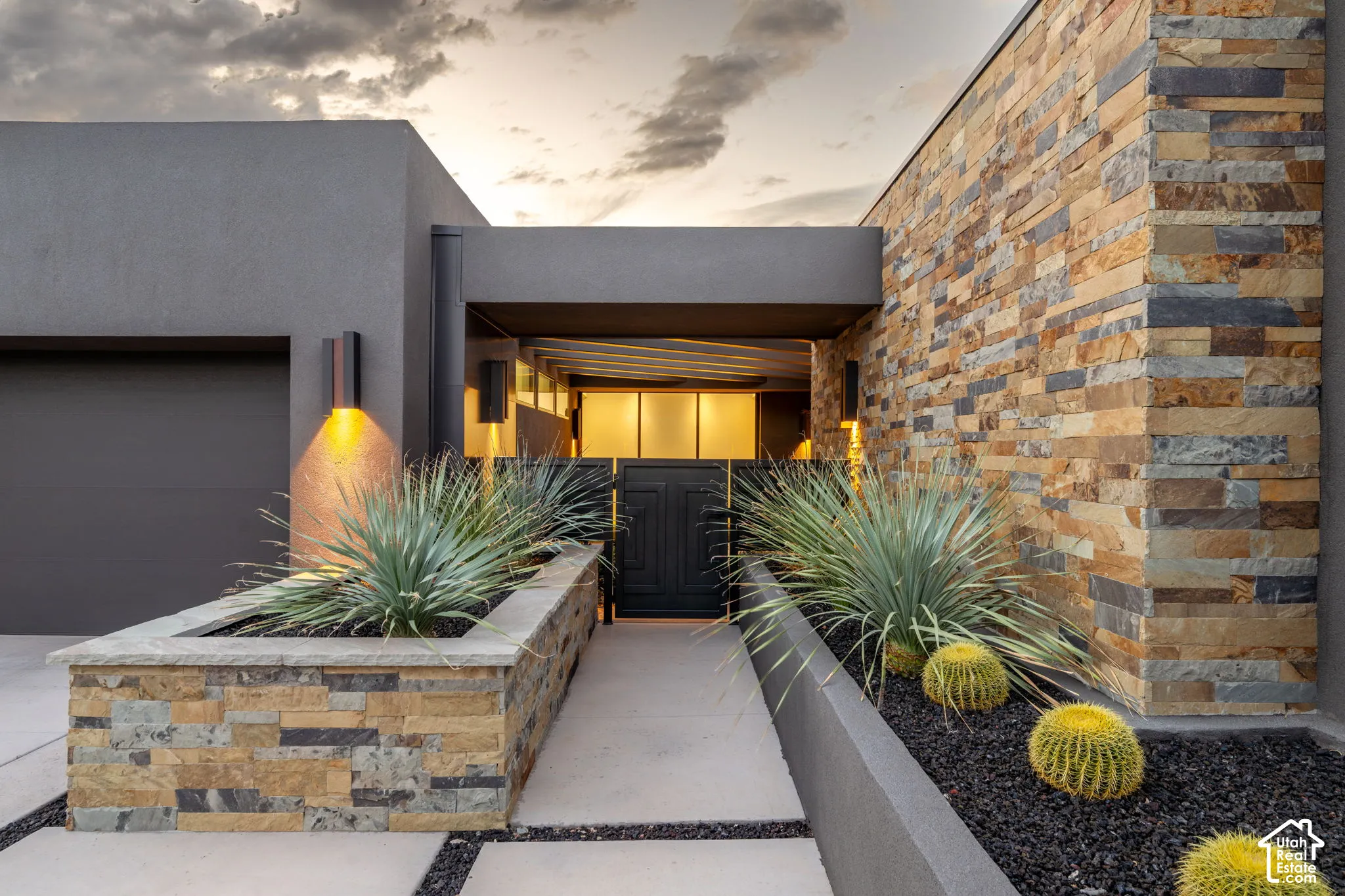 Modern exterior featuring stacked stone accents, smooth stucco finish, xeriscaped planters, and integrated wall-mounted lighting