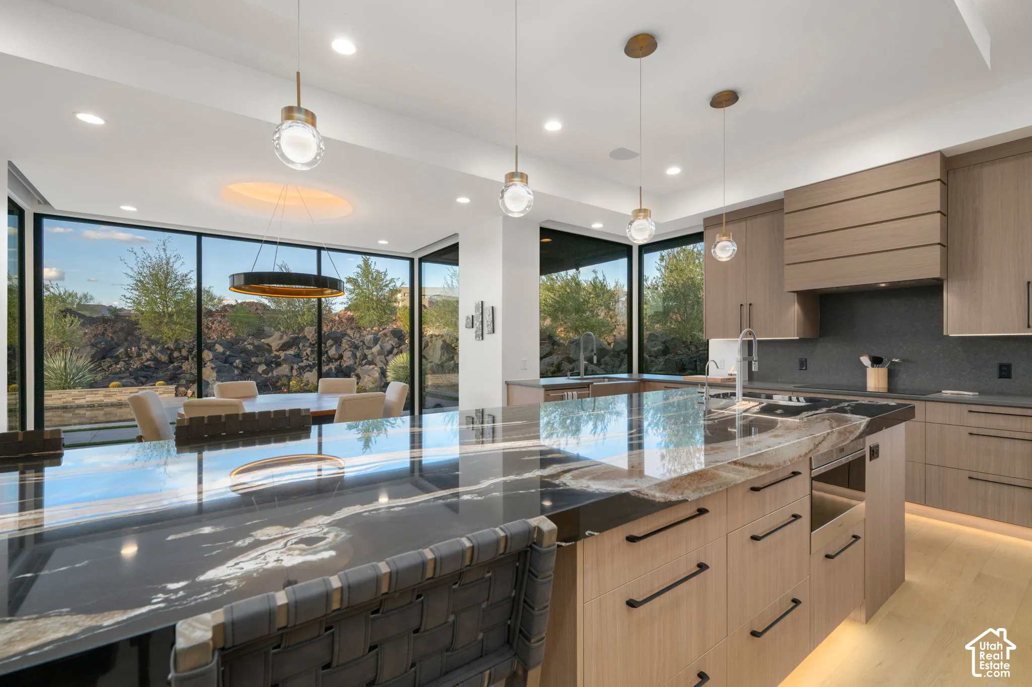 Modern kitchen featuring a large central island with stone countertop, floor-to-ceiling glass windows, flat-panel cabinetry, recessed lighting, and integrated pendant light fixtures
