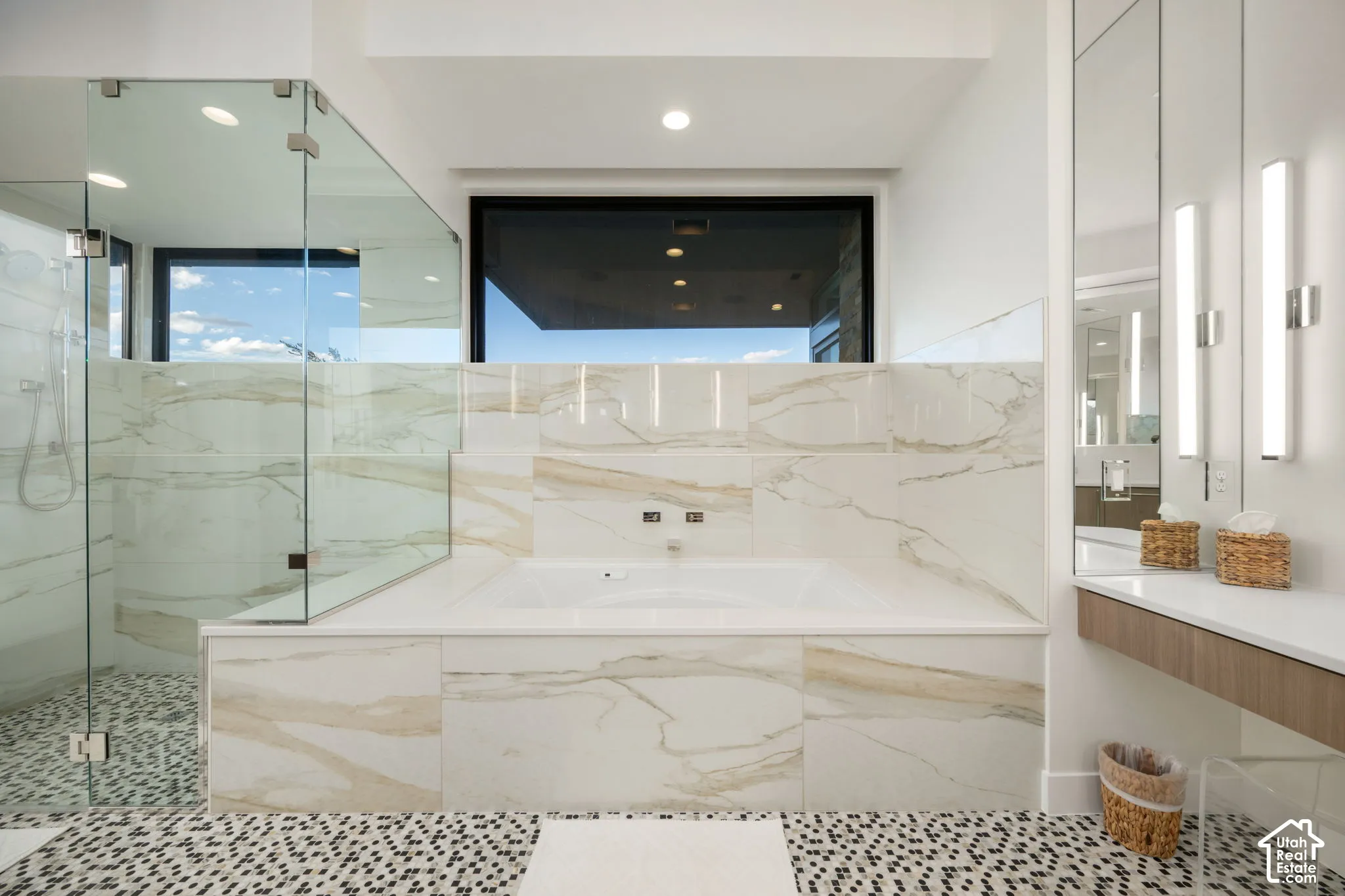 Large-format tile surround with integrated soaking tub, glass-enclosed shower, mosaic floor tile, floating vanity with surface-mounted sink, and wall-mounted light fixtures