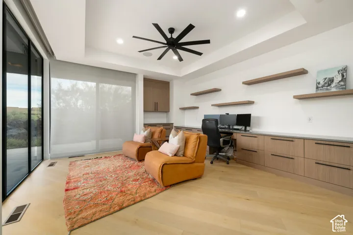 Custom office featuring wood-finish flooring, built-in cabinetry, floating wall shelves, a recessed ceiling, and floor-to-ceiling glass sliding doors