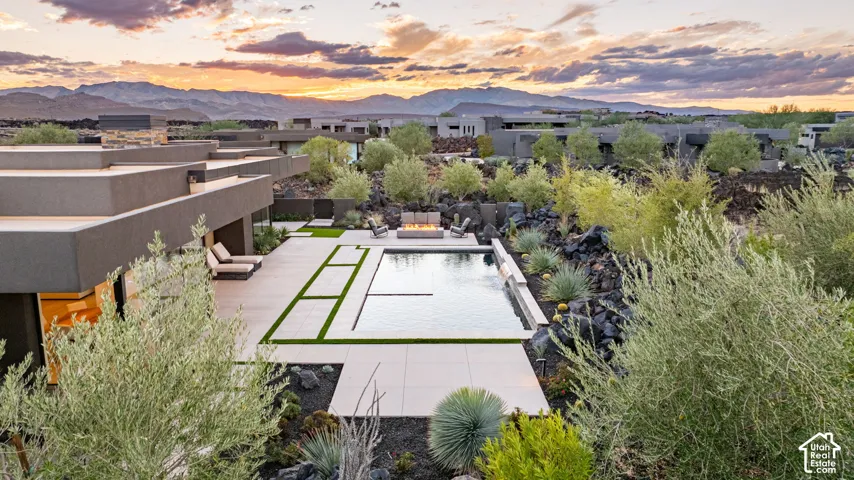 Contemporary residence featuring a rectangular swimming pool, integrated water feature, concrete paver patio, and low-maintenance desert landscaping set against a mountain backdrop