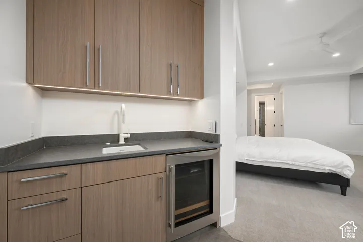 Built-in wet bar featuring wood-finish cabinetry, dark solid-surface countertop, under-cabinet lighting, integrated beverage refrigerator, and gooseneck faucet