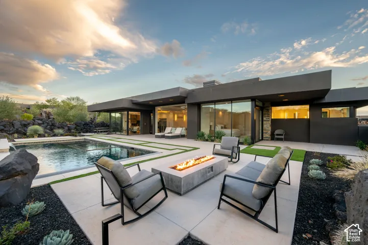 Modern desert-style outdoor space featuring a built-in concrete fire pit, a concrete-surfaced patio, in-ground swimming pool with waterfall feature, and native landscaping set against volcanic rock