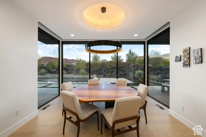 Modern dining space featuring floor-to-ceiling glass walls, light-toned wood-finish flooring, a recessed circular ceiling detail, and a prominent circular pendant light