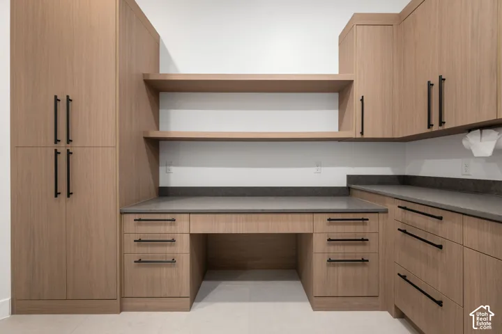 Custom wood-finish cabinetry featuring matte black hardware, integrated desk workspace, dual floating shelves, and dark solid-surface countertops