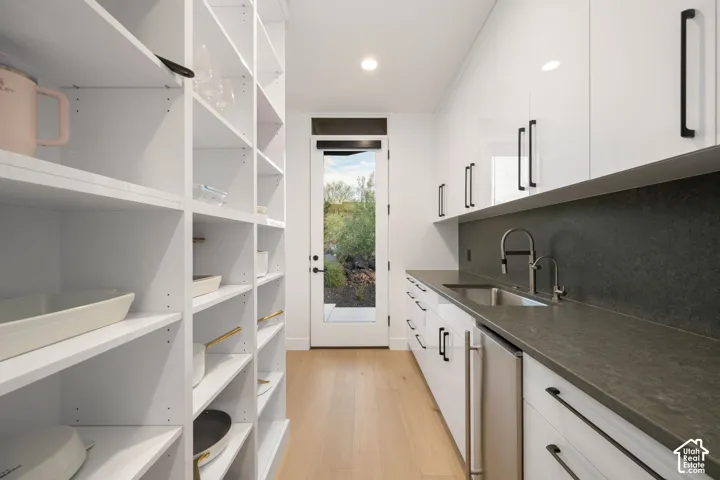Pantry featuring white cabinetry with matte black hardware, stone-finish countertops, wood-finish flooring, integrated sink, and glass-paneled exterior door